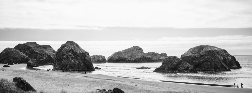 Black and white panoramic landscape photograph of huge rocks in the Pacific Ocean along the coastline of Oregon.