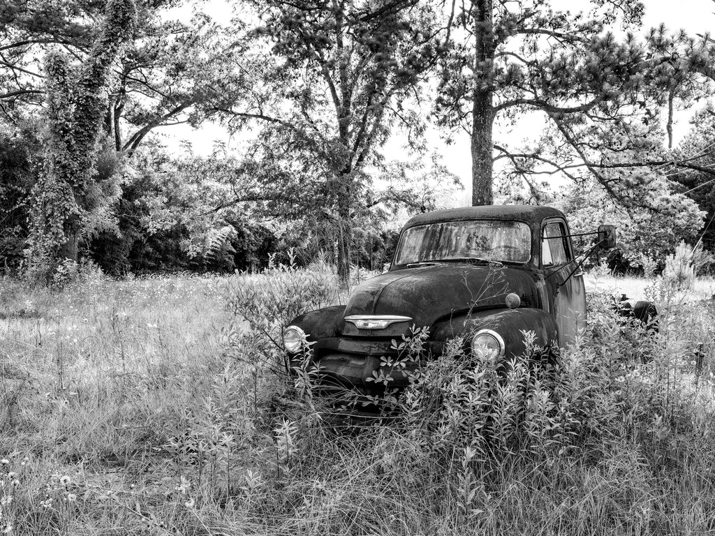 Black and white medium format photograph of an antique Chevrolet truck left abandoned in a field in the American South.