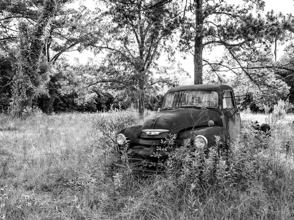 Black and white medium format photograph of an antique Chevrolet truck left abandoned in a field in the American South.