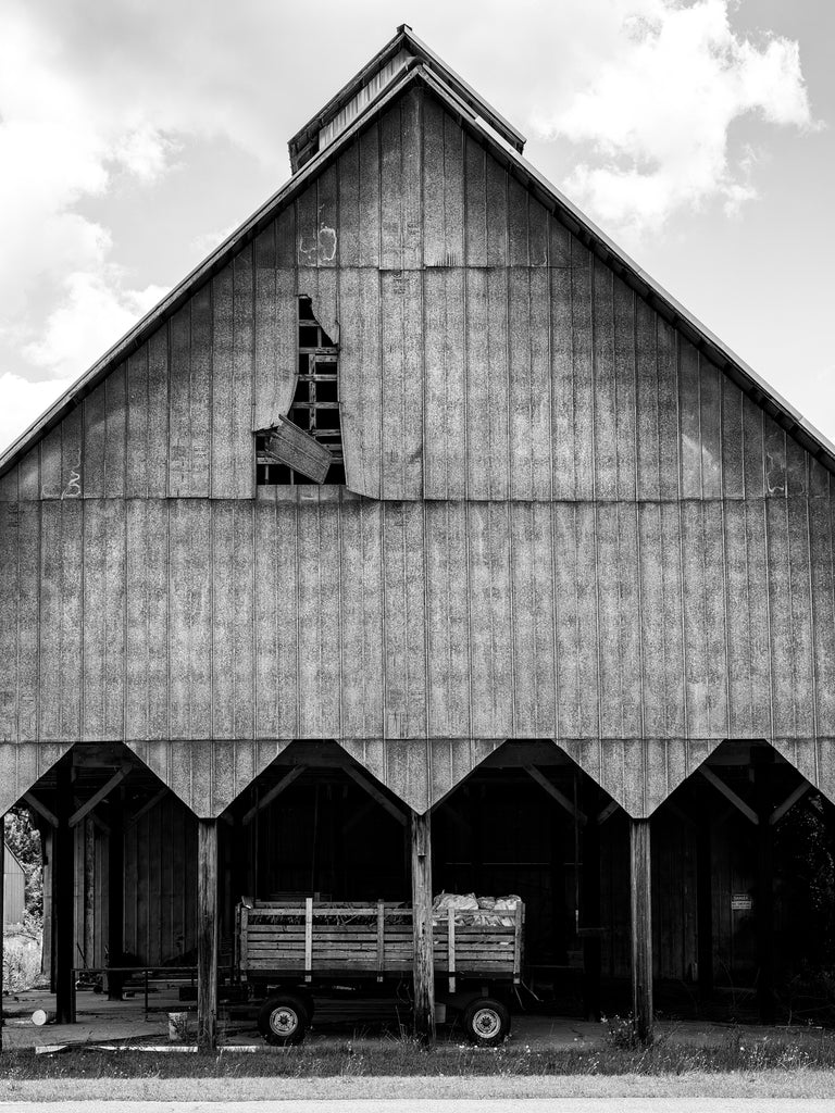 Black and white photograph of a barn in rural Leslie, Georgia with a steep roofline and a wagon parked in front.