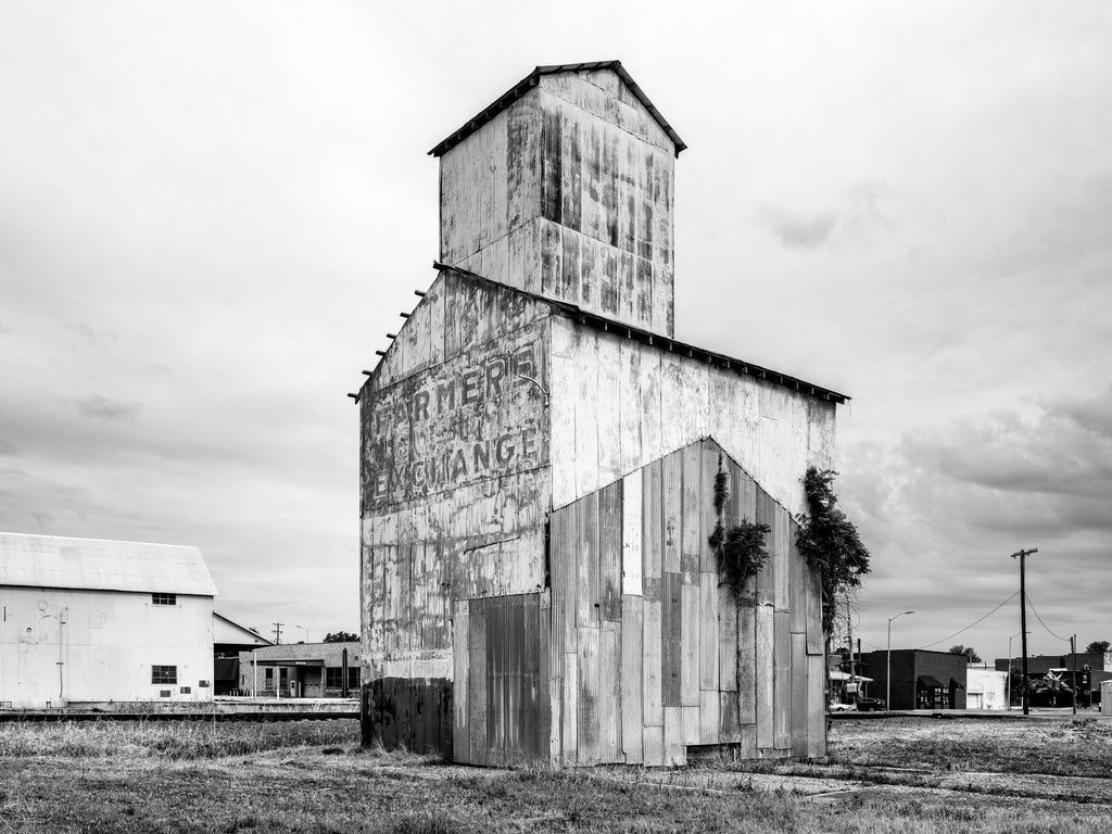 Black and white medium format photograph of an old grain elevator in a small town in Arkansas with the faded words Farmer's Co-Op Exchange painted on its side.
