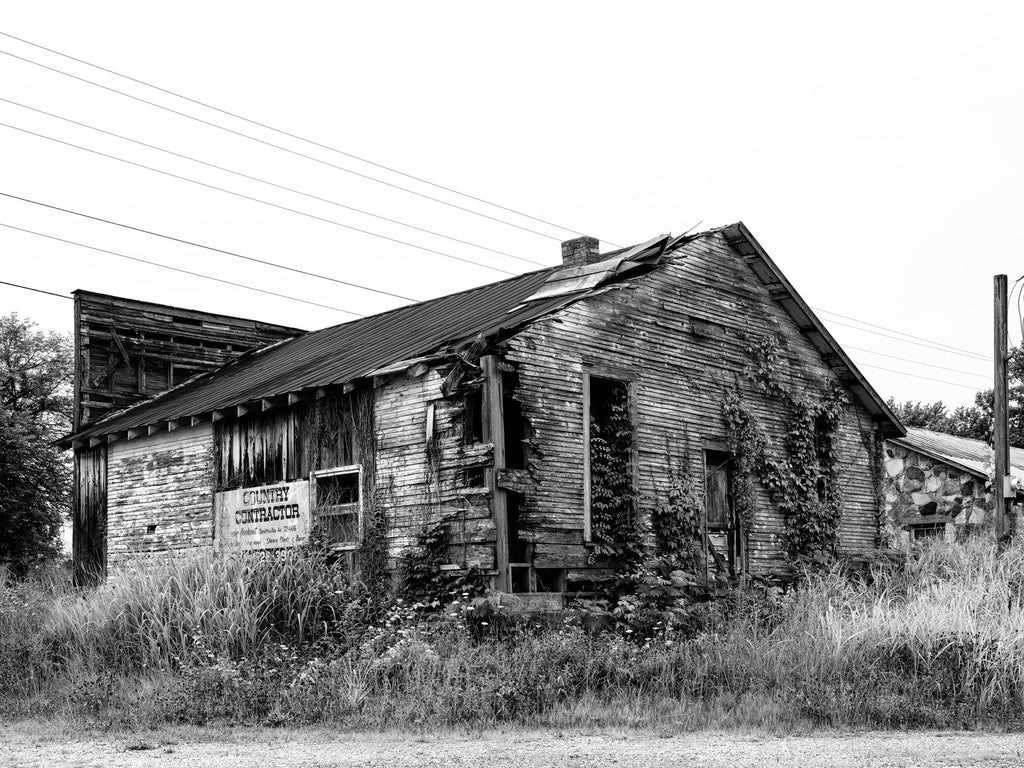 Black and white photograph of an abandoned wooden store building situated in tall grass along a back road in rural Arkansas.