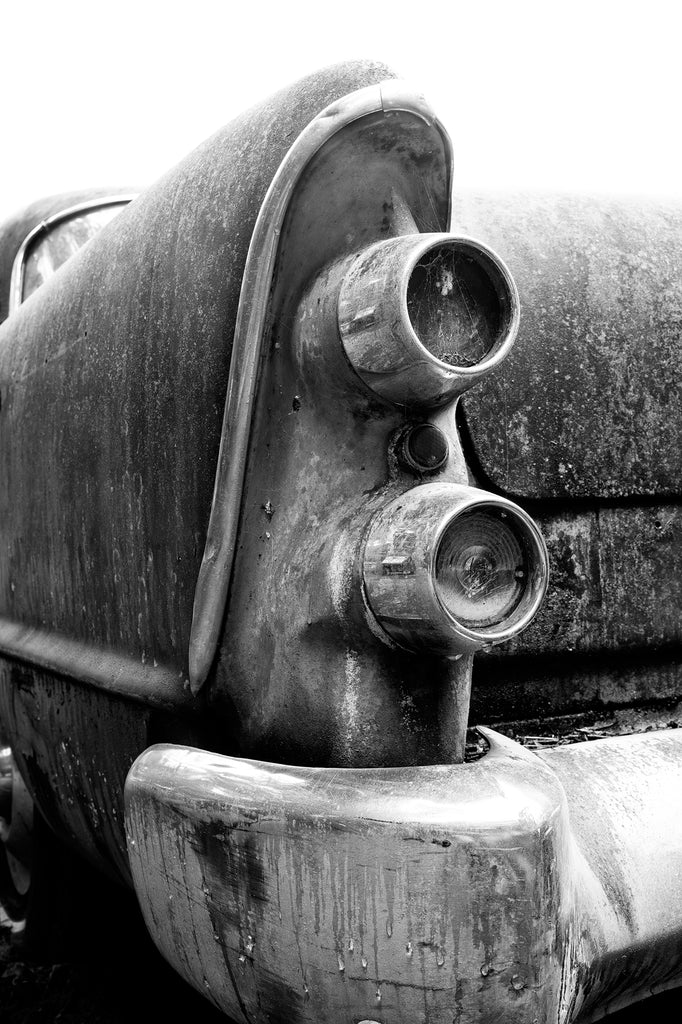 Black and white detail photograph of the tail lights on the rusty tail fin of a classic American automobile now abandoned as junk.