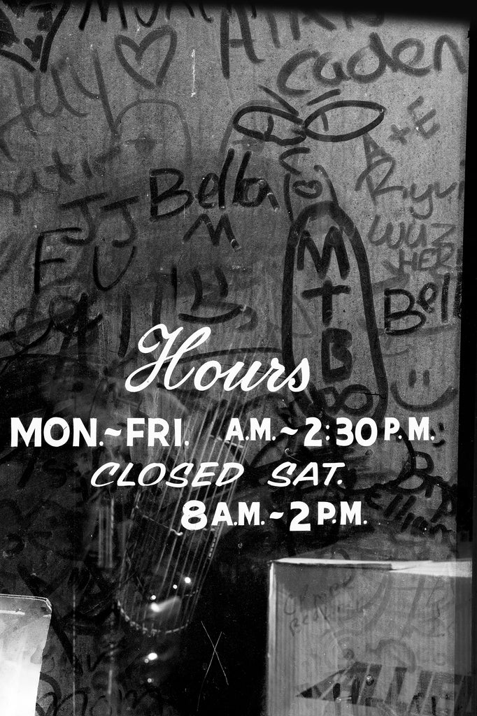 Black and white photograph of words written in the dust on the front door of an abandoned restaurant in a small town in the American South.
