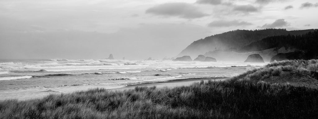 Black and white panoramic landscape photograph of morning mist across the sea stacks along the beautiful Oregon coastline at sunrise.