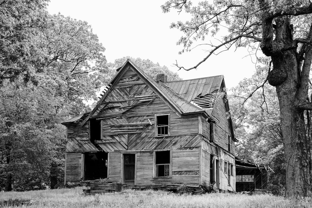 Black and white photograph of a large two-story abandoned farmhouse on the crest of a hill in the rural South.