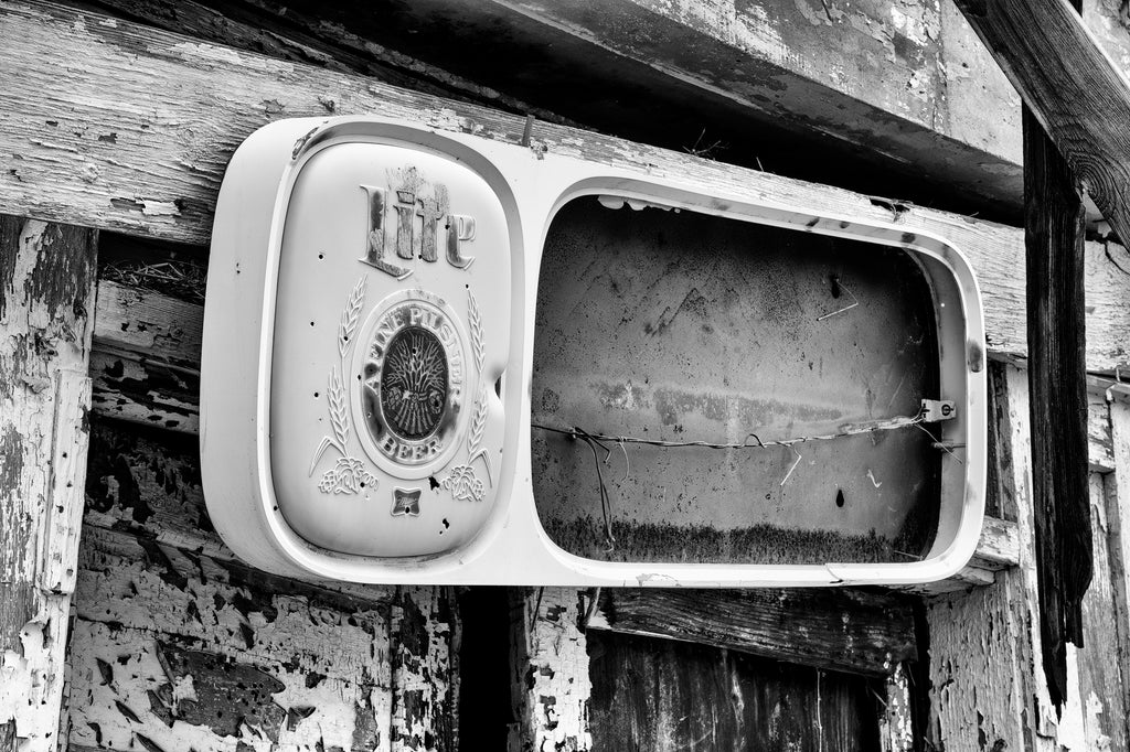 Black and white photograph of the broken old beer sign hanging over the front doors of the abandoned Last Chance Bar, which is also often called "the juke joint." The building began in 1903 as the Abe Lincoln Trading Company, selling groceries and other necessities in Clearview, Oklahoma.