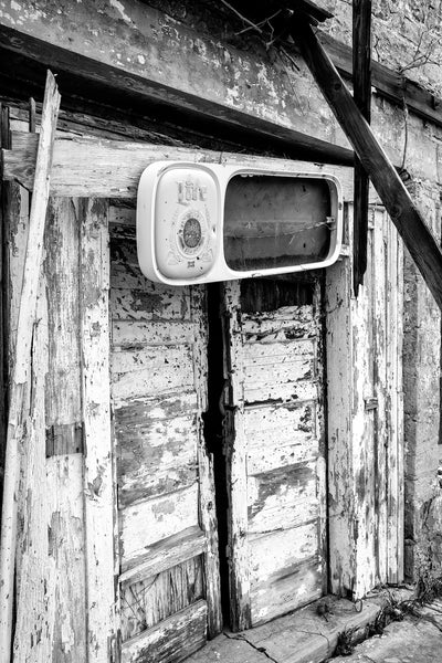 Black and white photograph of the weathered front doors and broken beer sign on the historic Last Chance Bar, built 1903 in Clearview, Oklahoma. The building which was added to the National Register of Historic Places in December, 2023, originally housed the Abe Lincoln Trading Company, a grocery and building supply store.