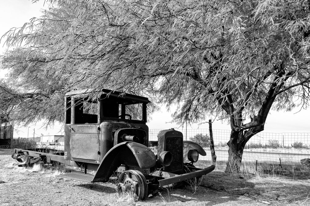 Black and white photograph of the rusty shell of an old truck parked along a discontinued alignment of Route 66 on the way to Oatman, Arizona.