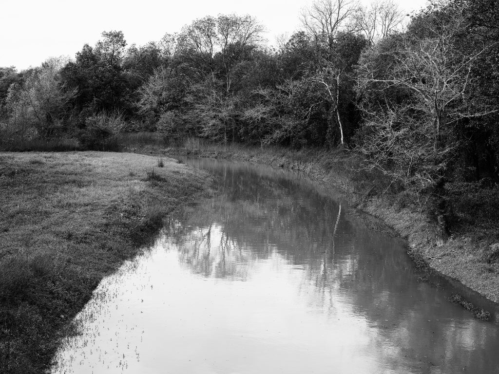 Black and white photograph of the slow rolling Hushpuckena River, namesake of the unincorporated community of the same name in Bolivar County, Mississippi.