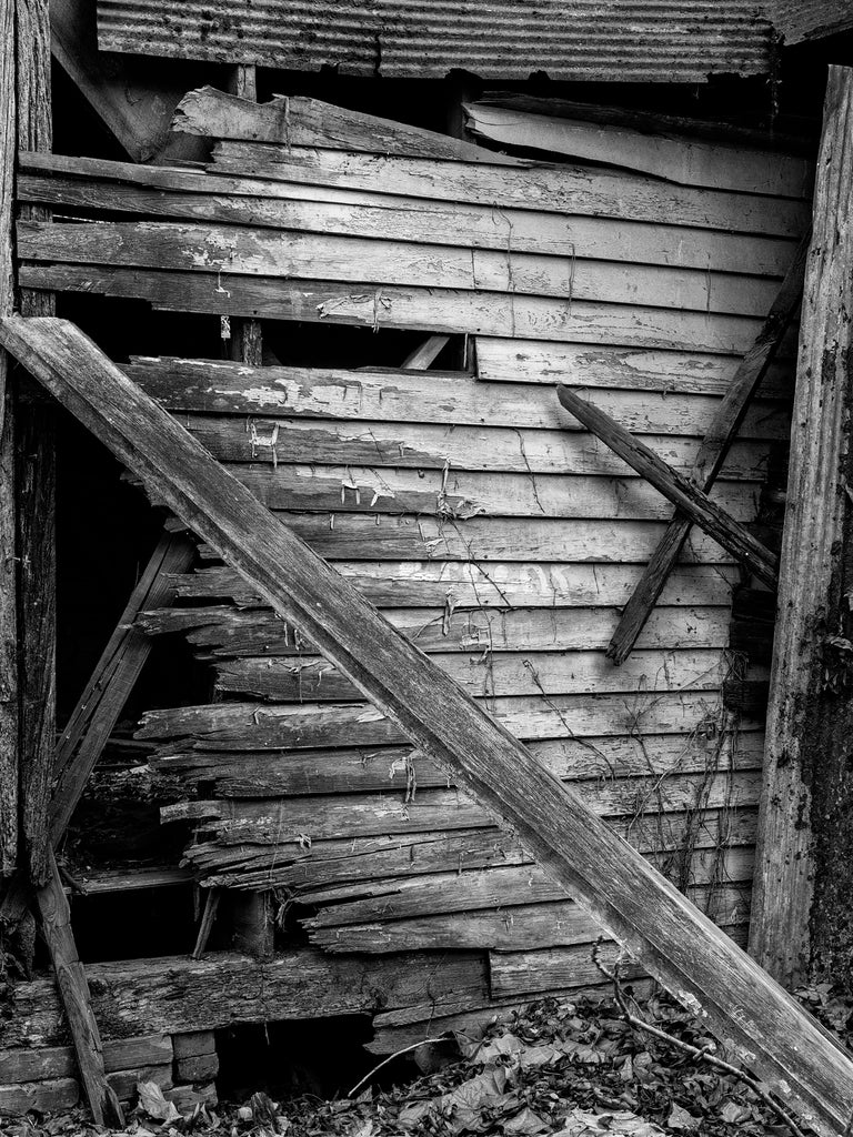 Black and white photograph of the rotting clapboards and fallen planks of an abandoned house in the ghost town at Hushpuckena, in the Mississippi Delta region.