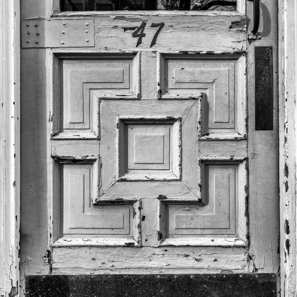 Black and white photograph of the rectangular designs of an old door on a storefront in a small New England town. (Square format)