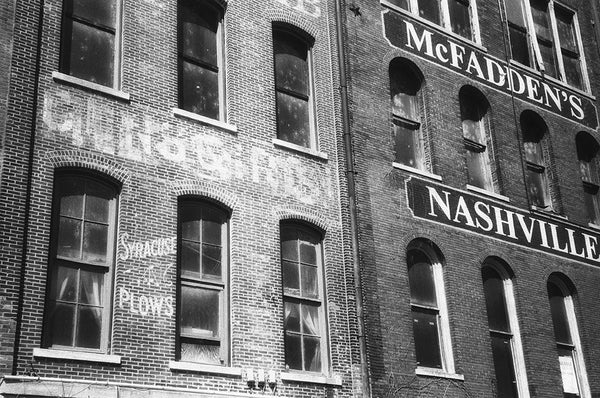 Black and white photograph of antique painted signs on the old brick walls of Nashville's riverfront. The turn-of-the-century sign for Syracuse Plows can be seen at bottom left.