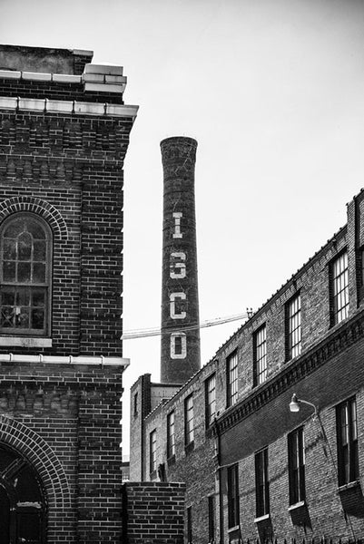 Black and white photograph of the old Lemp Brewery complex in St. Louis, Missouri. Once the 4th largest brewery in the US, construction on the complex began in 1865, and the brewery was sold due to financial and personal problems inside the Lemp family. At one point owned by ISCO, which left its name on the prominent brick chimney. The brewery complex was built over a natural cave system, with a cavern leading to the nearby Lemp Mansion.