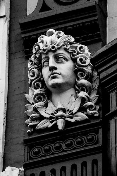 Black and white architectural detail photograph of classically-inspired, statue of a young man with curls in his long hair, on a building in downtown Philadelphia.
