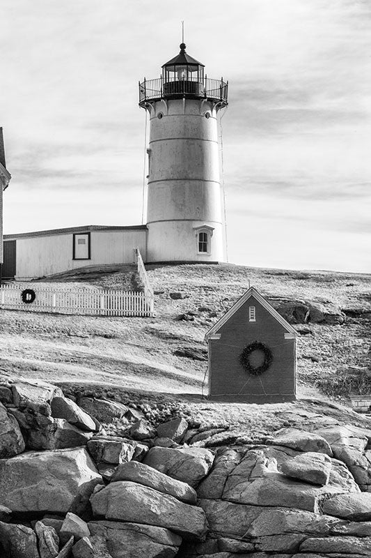 Black and white photograph of the beautiful Nubble lighthouse, which sits on a tiny island just yards off the coast at York, Maine. The lighthouse, officially called the Cape Neddick Lighthouse, began service in 1879 and is still in operation today. The lighthouse sits 88 feet above sea level atop the rocky Nubble islet.