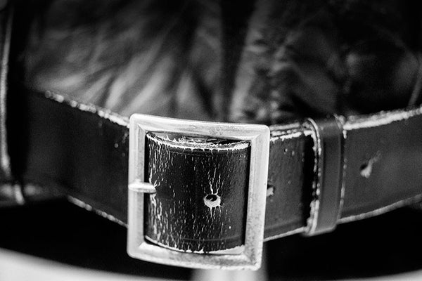 Black and white fine art photograph of a the silver buckle on a black leather jacket once owned and worn by Elvis Presley, seen in a museum exhibit.