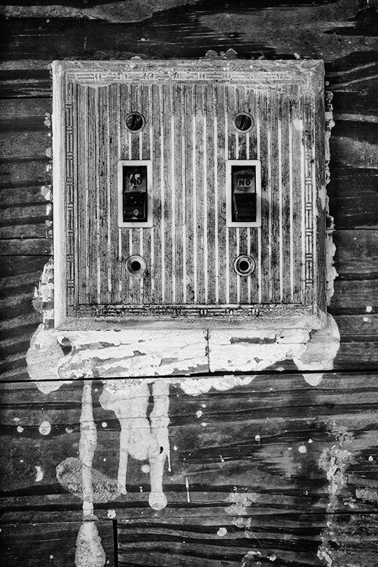 Black and white photograph of a grimy, old light switch plate surrounded by drips of white paint, inside the home of the late blues musician Sleepy John Estes in Brownsville, Tennessee.