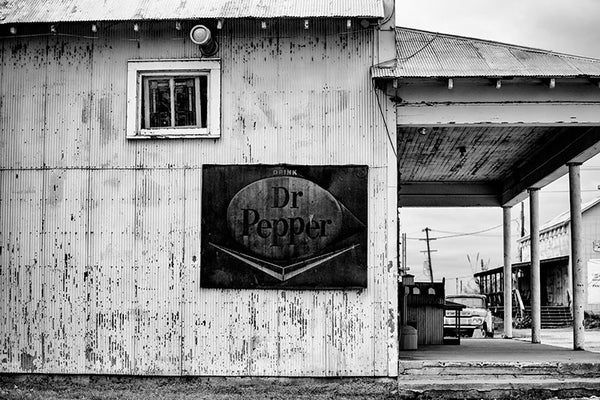 Black and white photograph of an old wood and corrugated steel building near Clarksdale, Mississippi, with a rusty vintage Dr. Pepper sign.