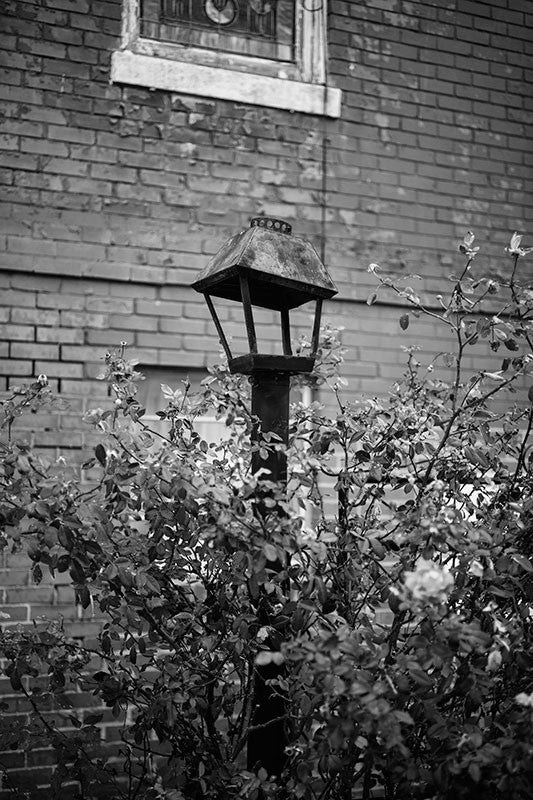 Black and white photograph of a dented lamp in the lawn of a historic red brick church in downtown Clarksdale, Mississippi.