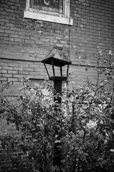Black and white photograph of a dented lamp in the lawn of a historic red brick church in downtown Clarksdale, Mississippi.