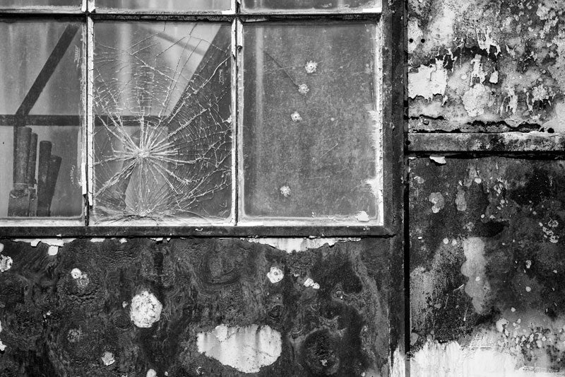 Black and white photograph of the cabin on an abandoned heavy machine suffering from neglect, with broken windows and rusty walls.