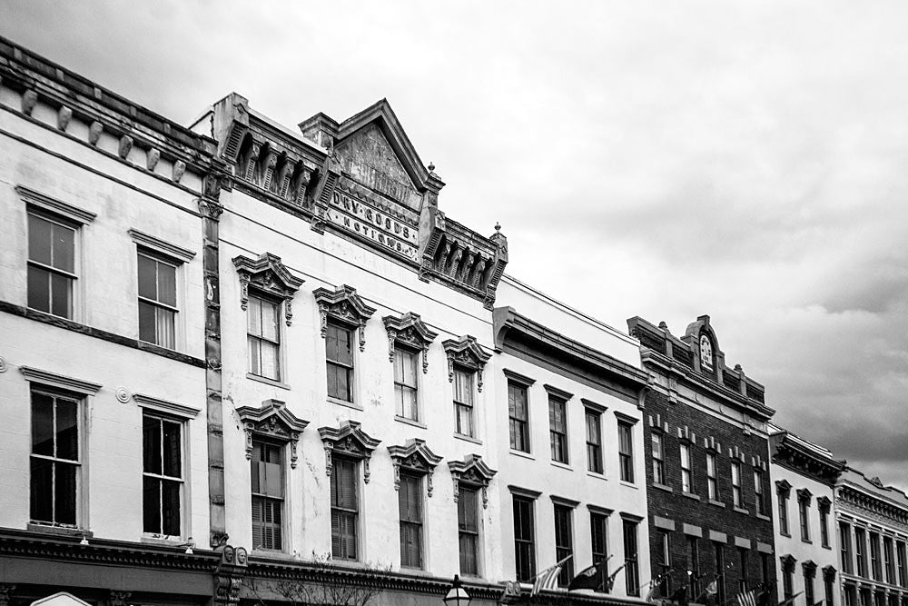 Black and white photograph of historic store fronts along Charleston's Meeting Street, with an antique, pressed metal sign that offers Dry Goods and Notions. 