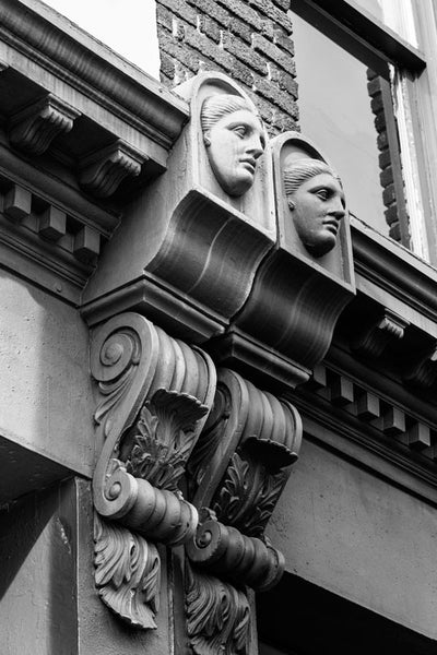 Black and white architectural detail photograph of female faces in the decorative scrollwork on buildings dating to the 1890s on Charleston's Meeting Street.