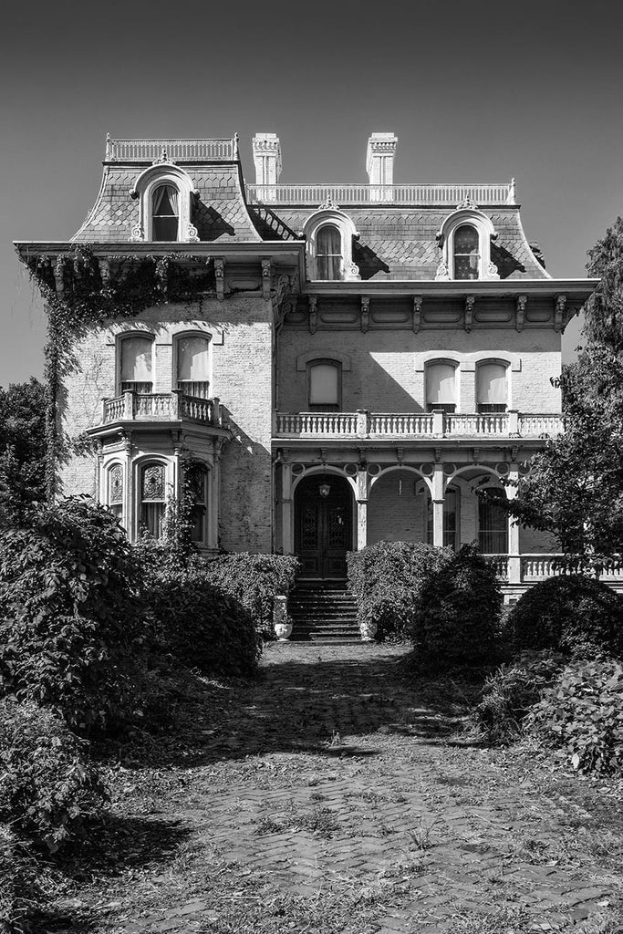 Black and white photograph of the front of Riverlore Mansion, a stately white home built in Cairo, Illinois in 1865 by a wealthy riverboat captain, who made his fortune on the two nearby rivers (the Ohio and Mississippi) that converge at Cairo. According to legend, the upper floor pilot's room was built to allow the captain to see the rivers from his home.
