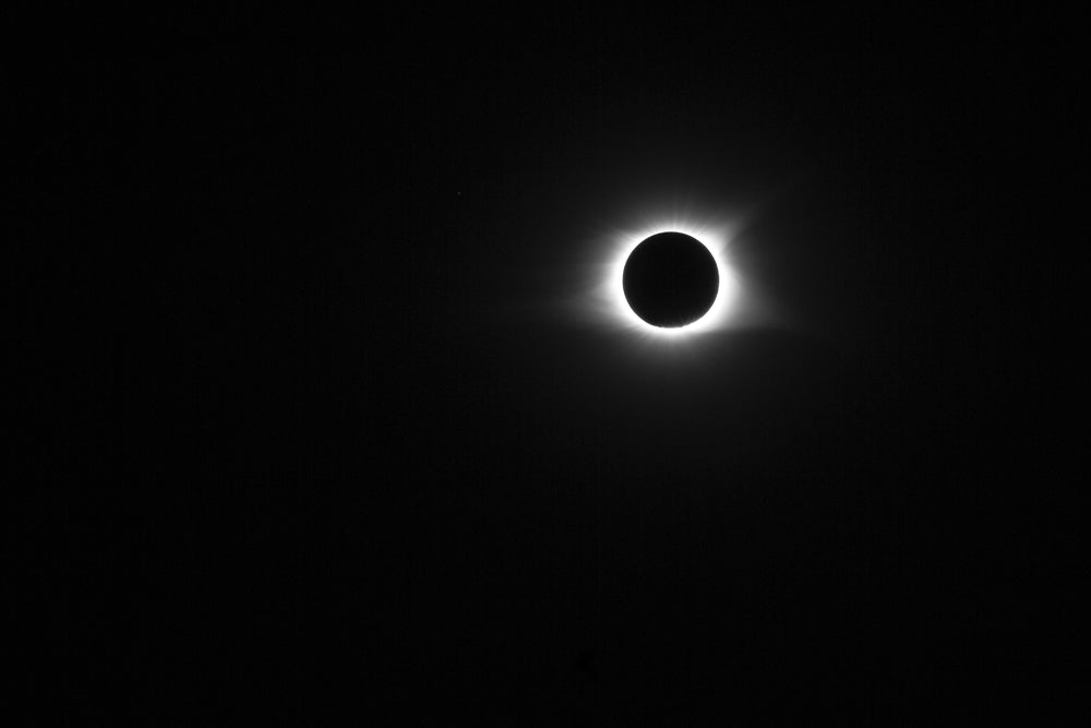 Black and white photograph of the sun in totality with its corona glowing around the moon during the great solar eclipse of 2017.