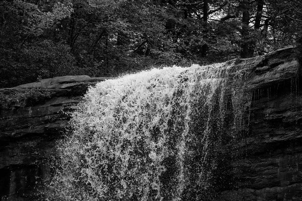 Black and white landscape photograph of the crest a waterfall in dramatic light, capturing individual water droplets in mid-air.
