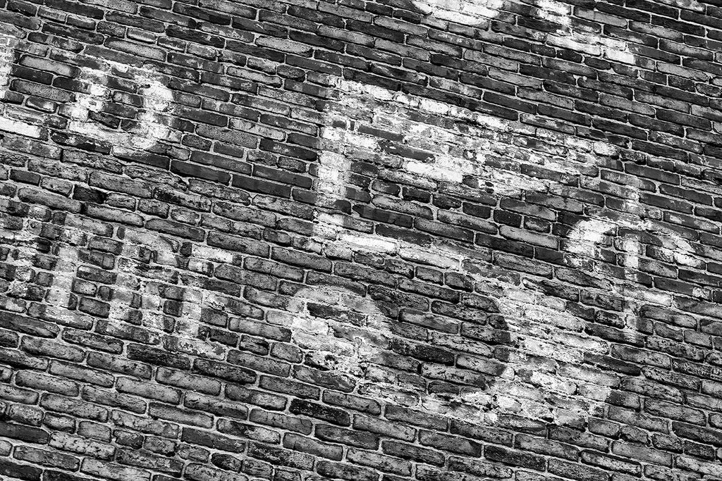 Black and white photograph of a fading five-cents "ghost sign," a historic advertisement that was painted on a brick wall many decades ago.
