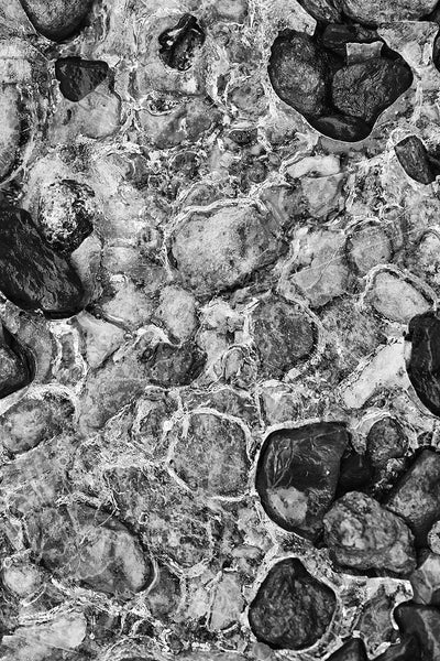 Black and white landscape photograph of sparkling frozen river ice across and around the stones in the stream bed.
