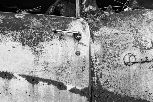 Black and white fine art detail photograph of the rusty driver's side door on a classic American car, junked and abandoned in the forest.