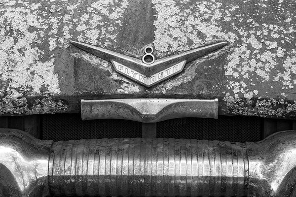 Black and white fine art detail photograph of the large, chrome ornament on the rusty hood of a classic, antique Plymouth V8.
