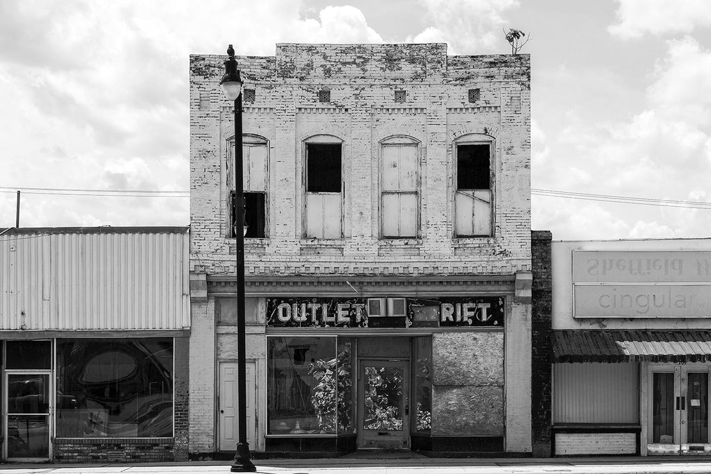 Black and white photograph of an abandoned two-story storefront with trees growing inside the building.