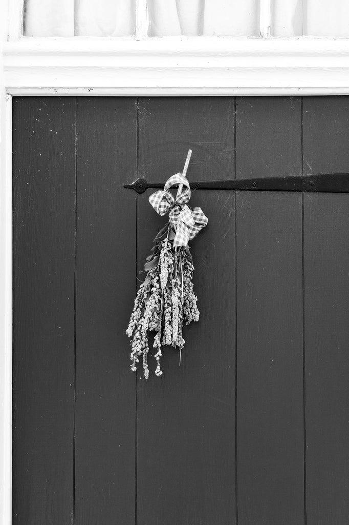 Black and white architectural detail photograph of an old door with a hanging of dried flowers on a historic house in beautiful Ste. Genevieve, Missouri.