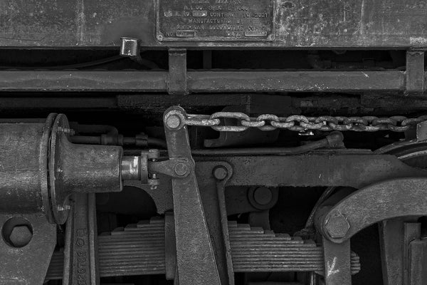 Black and white photograph of the mechanical parts on the undercarriage an old railroad car, creating a black on black tonal effect.