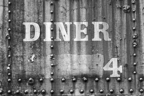 Black and white photograph of an abandoned railroad dining train car with the words "Diner 4" on its exterior wall