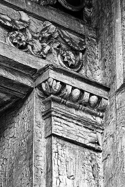 Black and white architectural detail photograph of beautifully decorative woodwork on the front of a big abandoned white house in New Orleans.