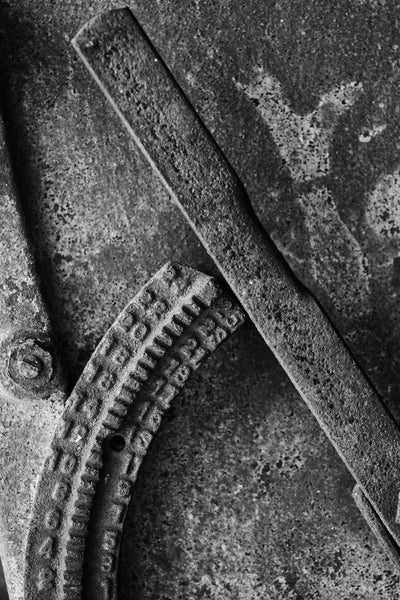 Black and white photograph of a rusty handle on an antique farm machine with a numbered gauge.