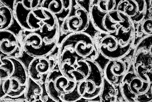 Black and white detail photograph of a white cast iron bench in an unkept section of Savannah's famous, beautiful, and creepy Bonaventure Cemetery.