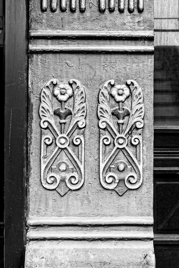 Black and white photograph of ornate cast iron flowers seen on an old building on the main street of a small town. 