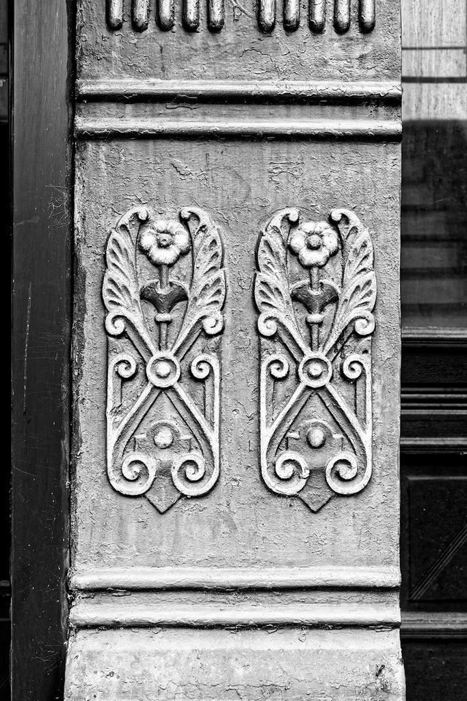 Black and white photograph of ornate cast iron flowers seen on an old building on the main street of a small town.