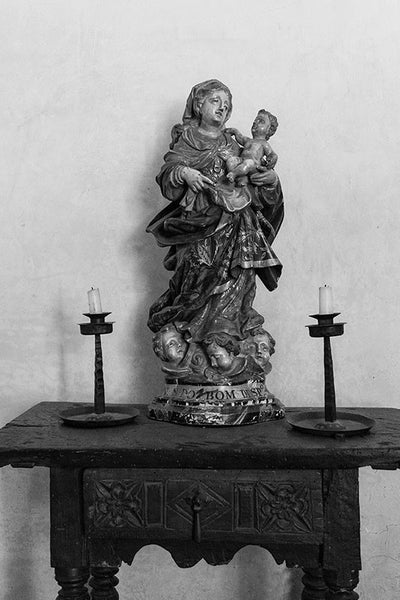 Black and white fine art photograph of the Madonna with Child on an antique Spanish table, between two unlit candles.