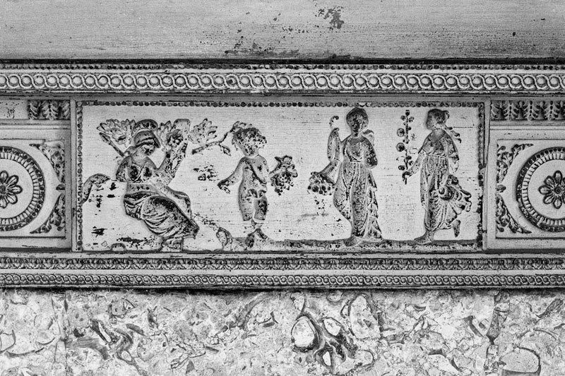 Black and white photograph of one of the scuffed antique fireplace mantels inside Drayton Hall, featuring classically-inspired figures.