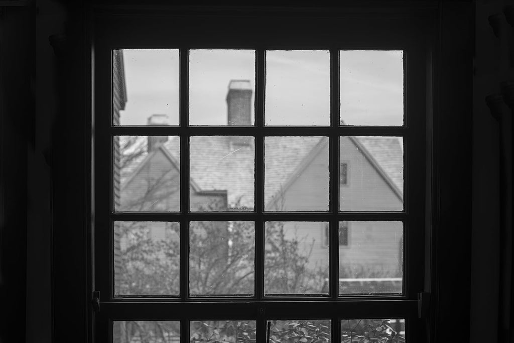 Black and white photograph of the historic "House of Seven Gables" as seen through the window of the Hawthorne house. Both iconic New England mansions are hundreds of years old.