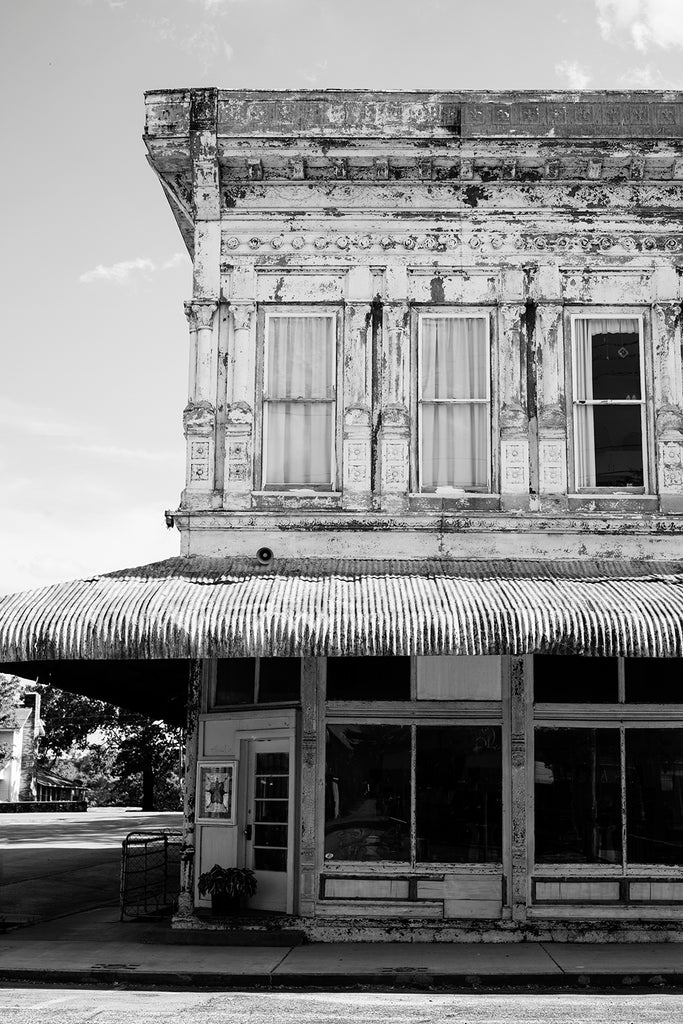Black and white photograph of a historic small town mercantile storefront with decorative metal exterior and a corrugated tin awning.