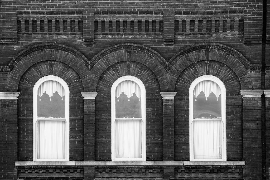 Black and white architectural photograph of three windows set into beautifully detailed brick work on the second story of a small town storefront