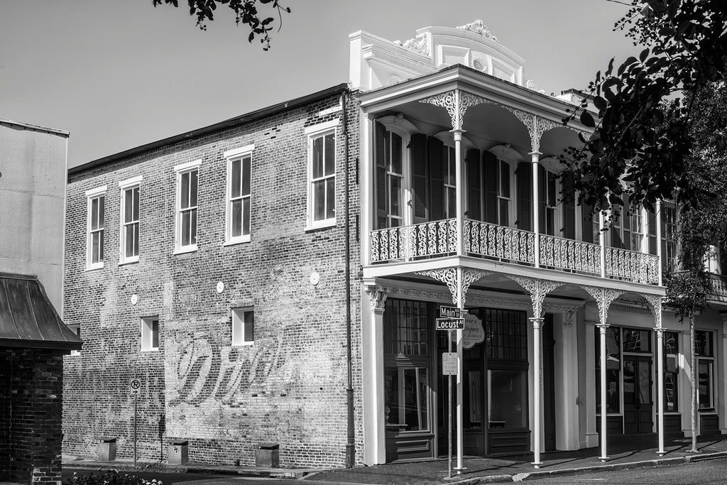 Black and white photograph of historic, ornate ironwork and a fading wall ad on Main Street at Locust in beautiful downtown Natchez, Mississippi.